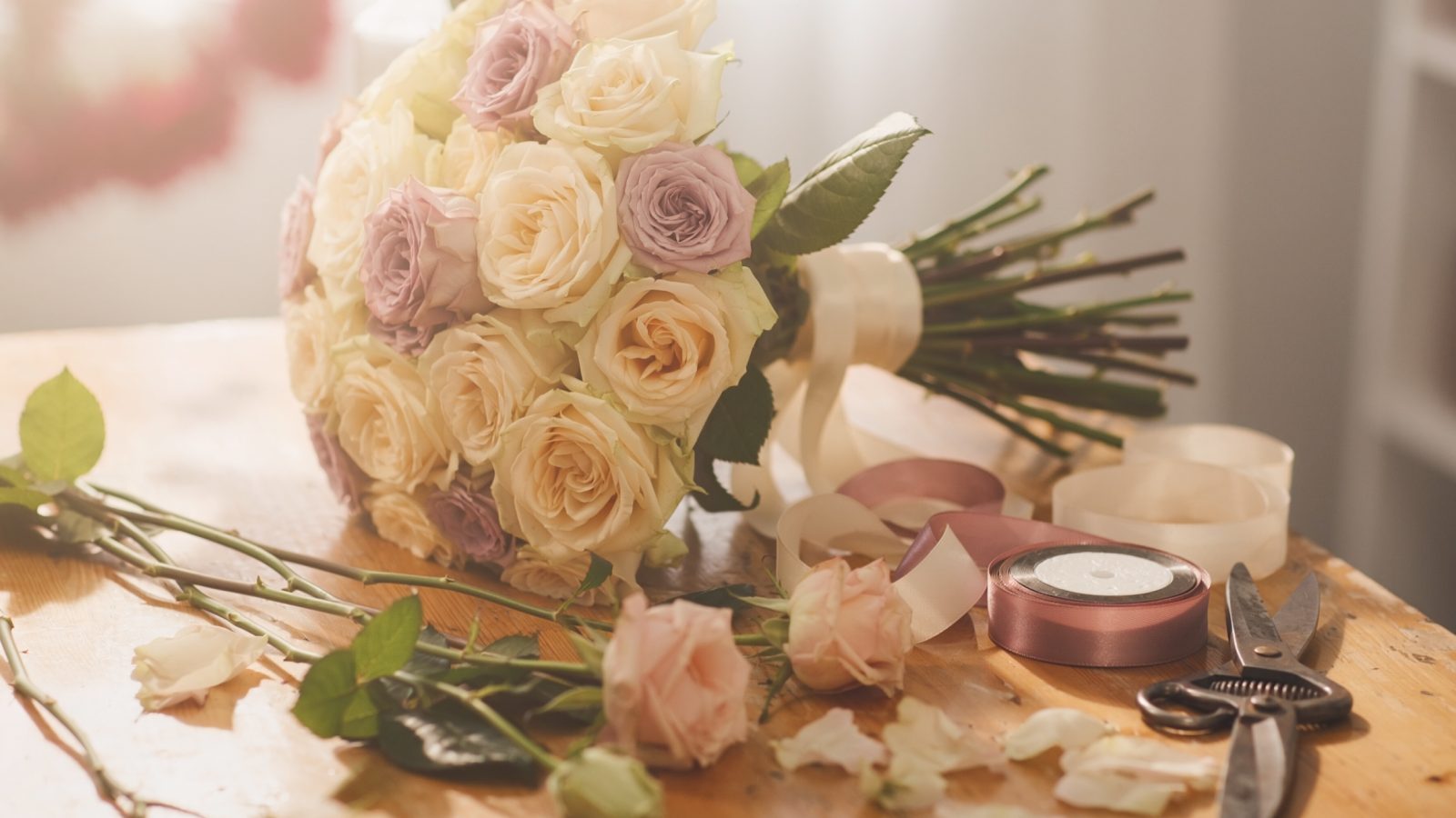 Werkbank einer Floristin mit halbfertigem Brautstrauß aus Rosen in Creme und Rosé