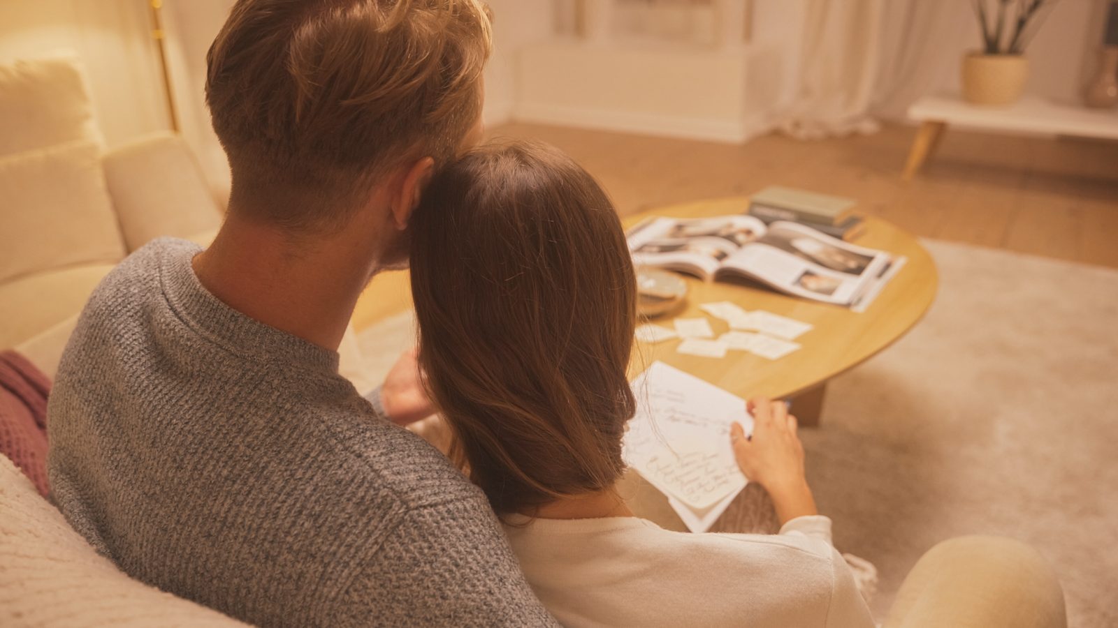 Paar plant abends auf dem Sofa seine Hochzeit mit Notizen und Magazin