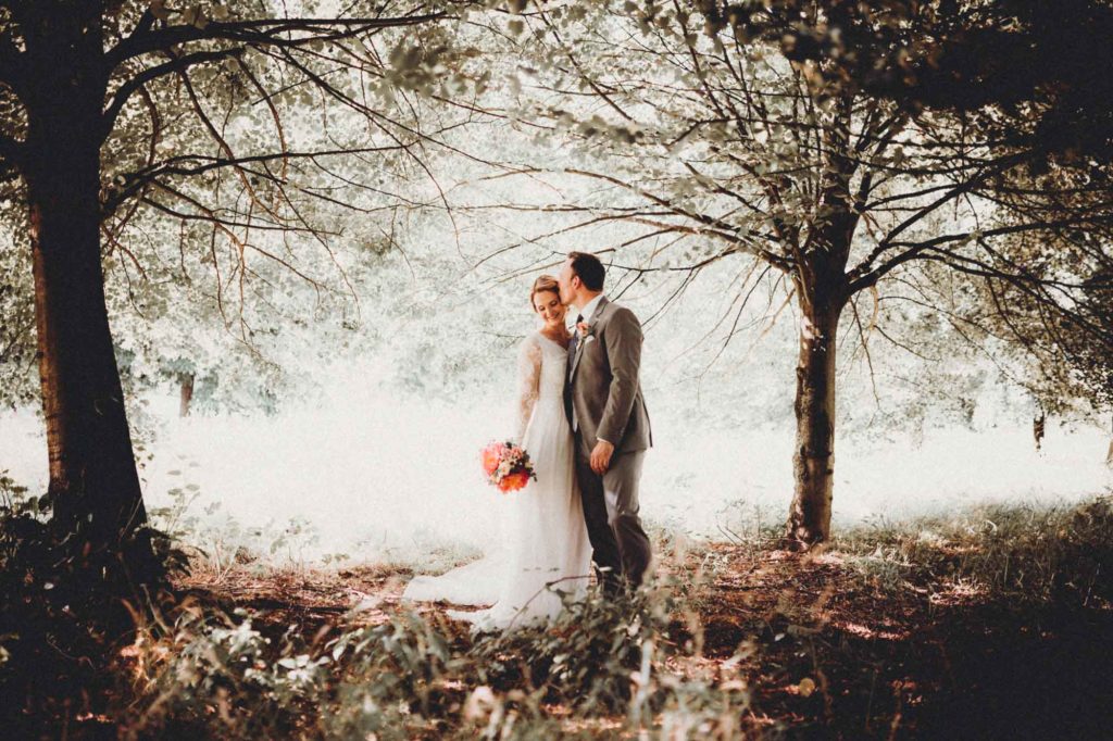 Braut im Hochzeitskleid und Bräutigam in Anzug bei einer romantischen Trauung im Freien unter zwei Bäumen