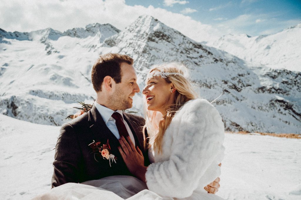 Ein Brautpaar in Hochzeitskleidung, umgeben von schneebedeckten Bergen, feiert ihre Trauung.