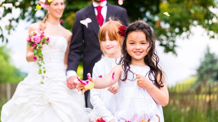 Hochzeitspaar in Hochzeitskleidung mit Blumenmädchen, umgeben von Hochzeitsdekoration im Freien während der Zeremonie.