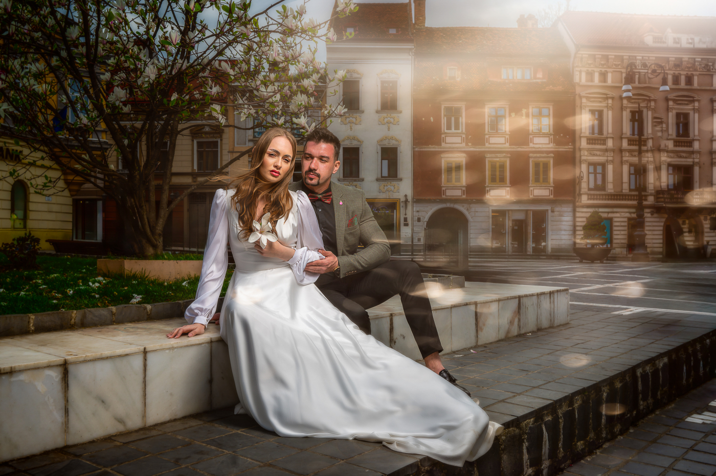 Braut und Bräutigam in eleganter Hochzeitskleidung posieren vor historischer Stadtlandschaft.