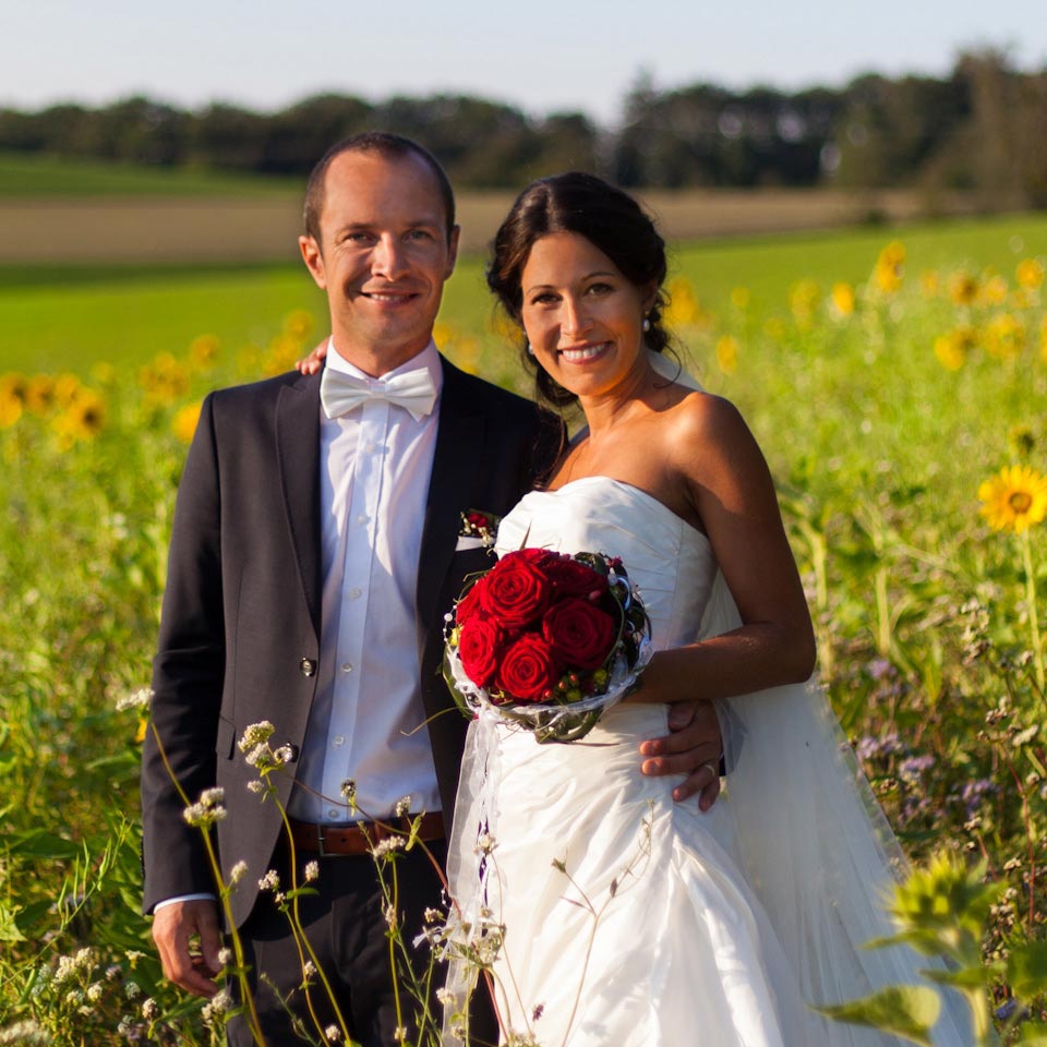 Braut und Bräutigam in schicker Hochzeitskleidung posieren im Sonnenblumenfeld bei ihrer Outdoor-Hochzeitszeremonie.