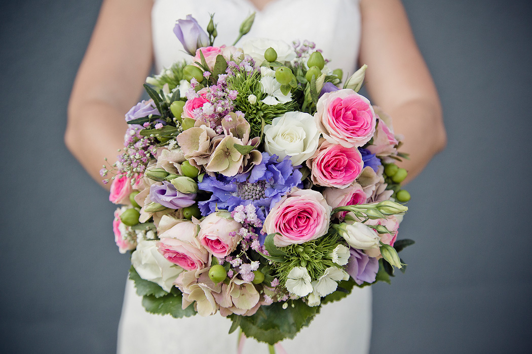 Die Braut hält einen wunderschön arrangierten Blumenstrauß mit rosa, lila und weißen Blüten bei der Hochzeit.