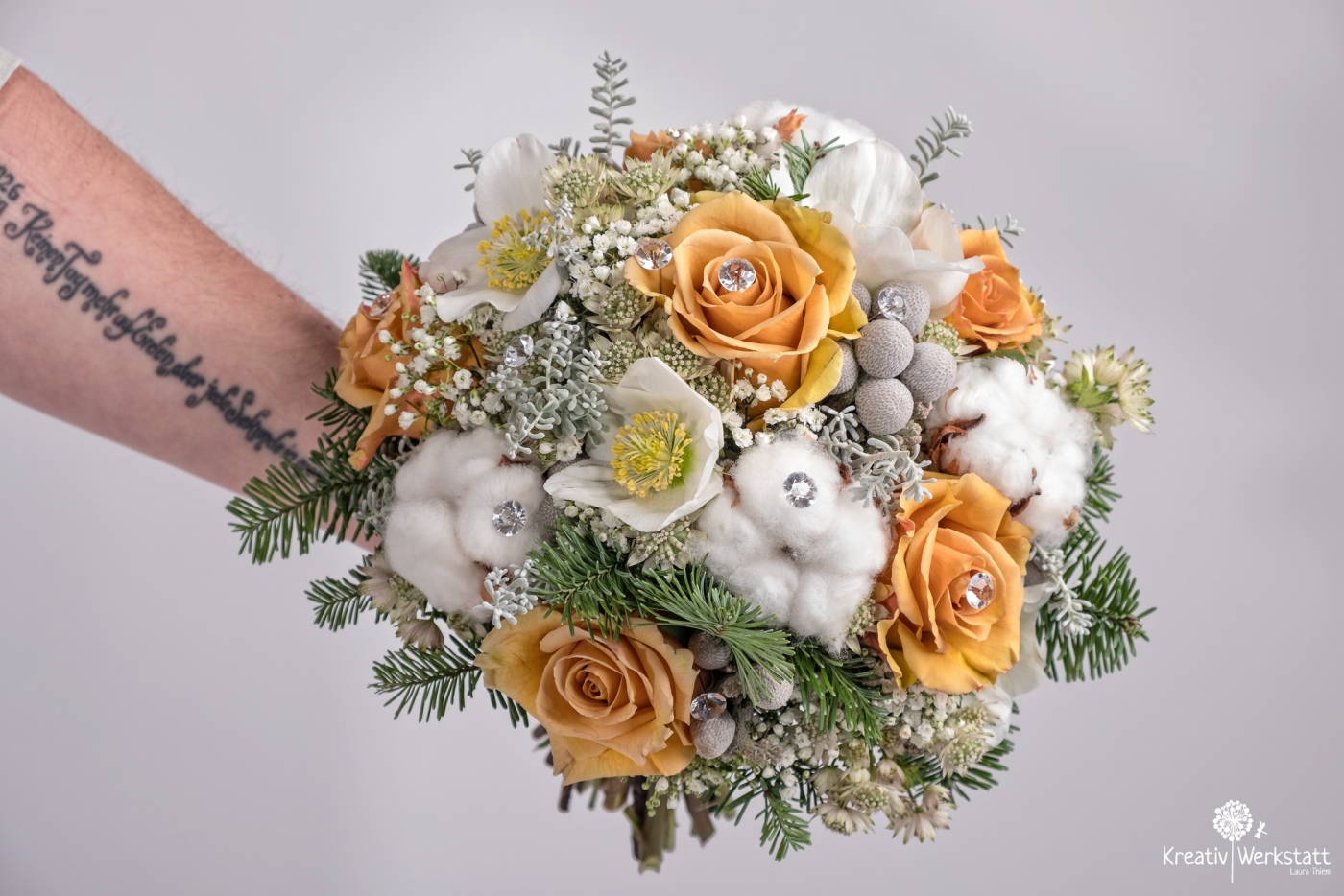 Nahaufnahme eines Brautstraußes mit orangefarbenen Rosen und weißen Blumen, gehalten von der tätowierten Braut.