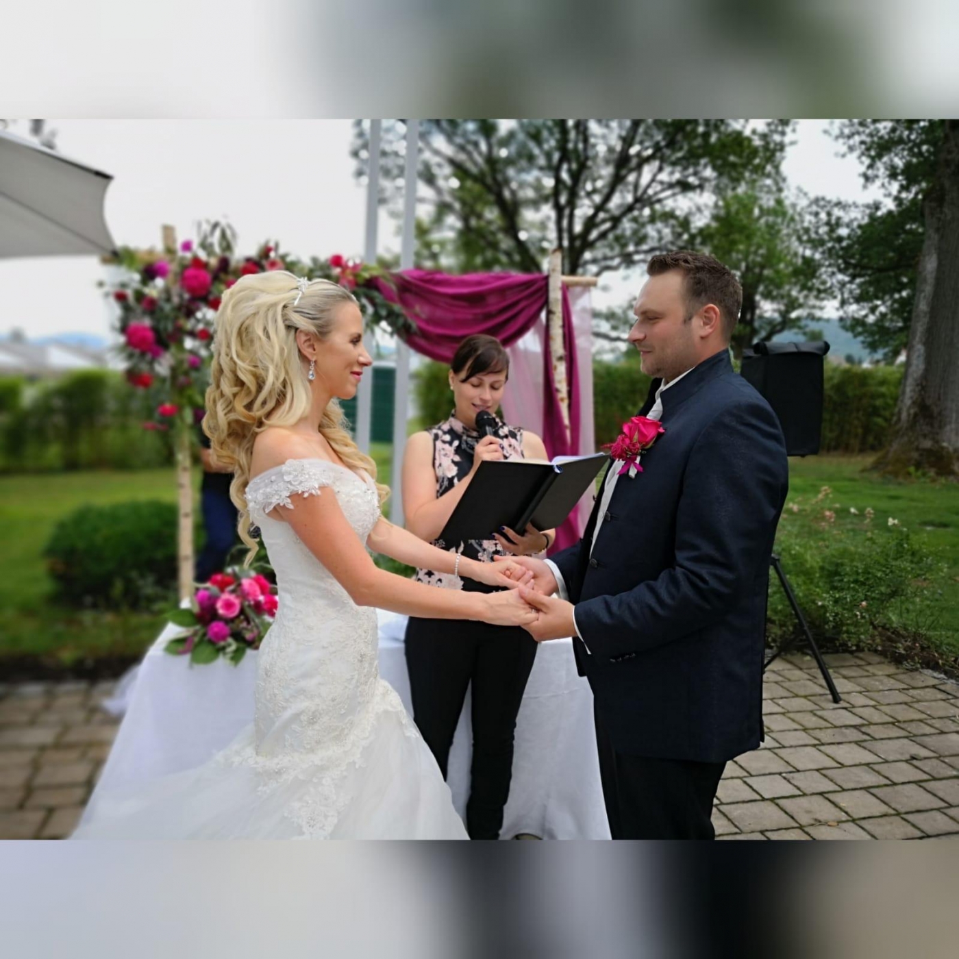 Braut und Bräutigam tauschen bei einer Hochzeitszeremonie im Freien Ringe, Hochzeitskleid und Dekoration im Hintergrund.