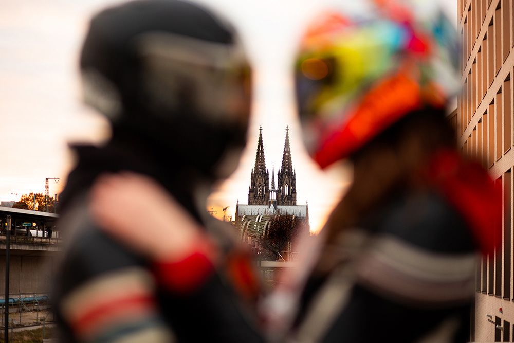 Verliebtes Brautpaar auf Motorrädern vor dem Kölner Dom, perfekte Hochzeitsidee für Motorradliebhaber.