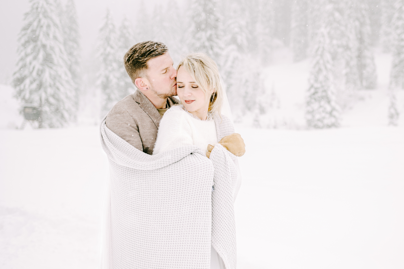 Braut und Bräutigam bei einer Winterhochzeit in verschneiter Landschaft, in Decken gehüllt, mit festlicher Stimmung.