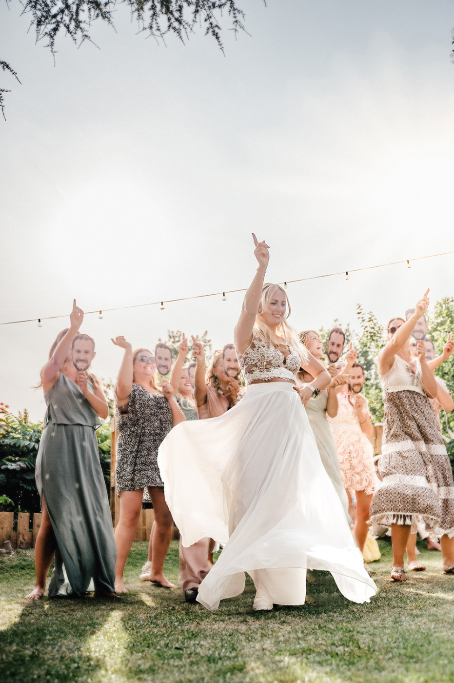 Braut tanzt im Hochzeitskleid auf der Grünen Wiese, umgeben von lachenden Brautjungfern und Gästen bei der Hochzeitsfeier im Freien.