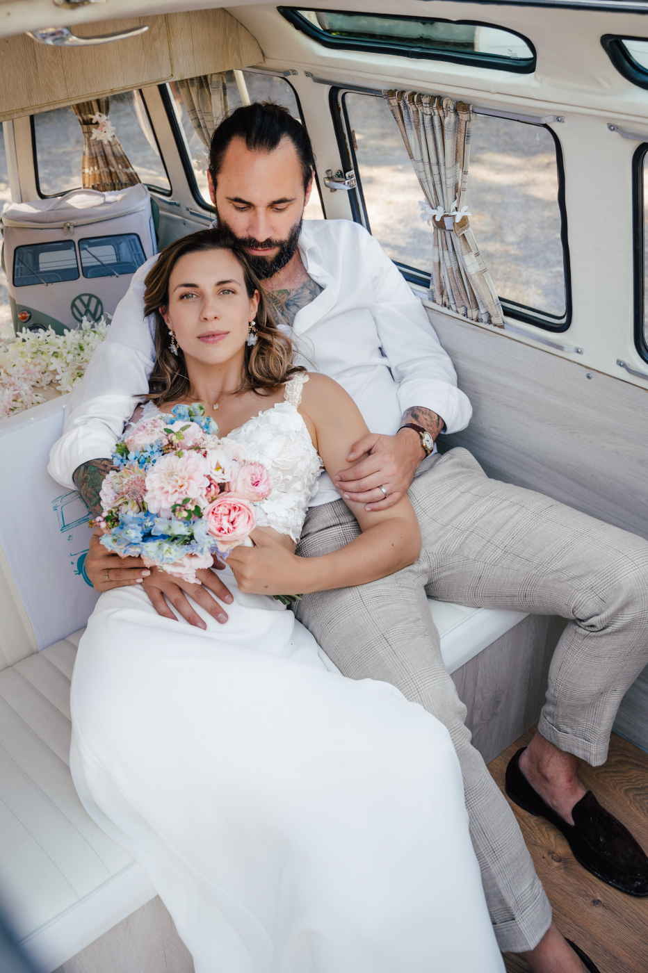 Braut im Hochzeitskleid und Bräutigam in einer gemütlichen Hochzeitslocation, umarmend auf einer Sitzbank, umgeben von Hochzeitsdekoration.