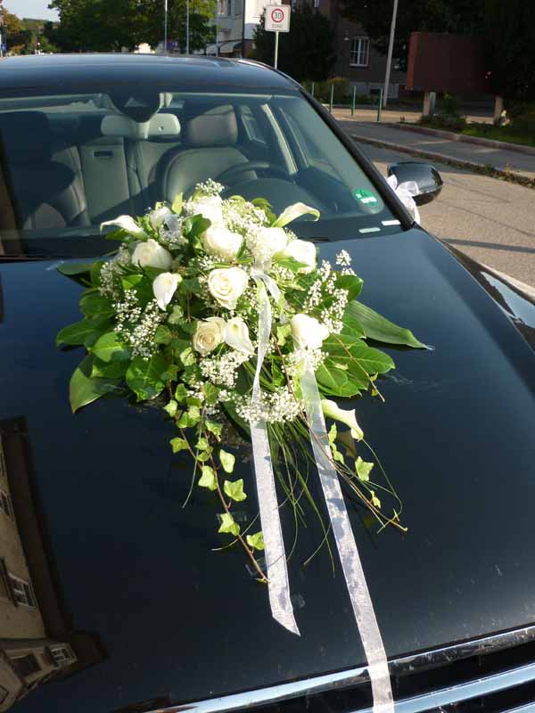 Blumenarrangement mit weißen Rosen und Schleifen auf der Motorhaube eines Hochzeitsautos, ideale Hochzeitsdekoration.