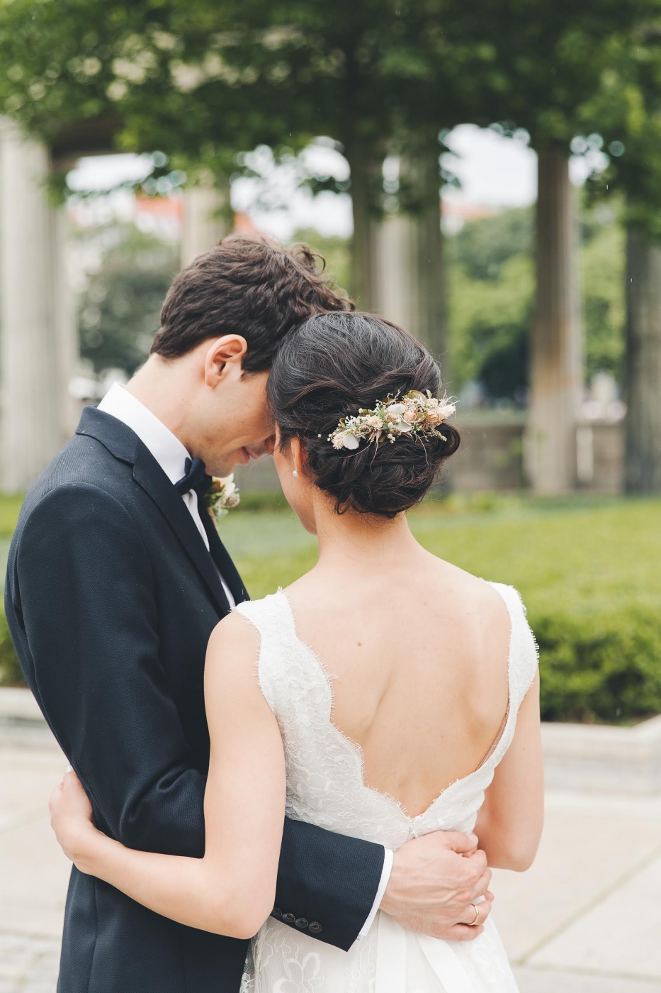 Braut und Bräutigam umarmen sich in einem Garten, die Braut trägt ein elegantes Hochzeitskleid.