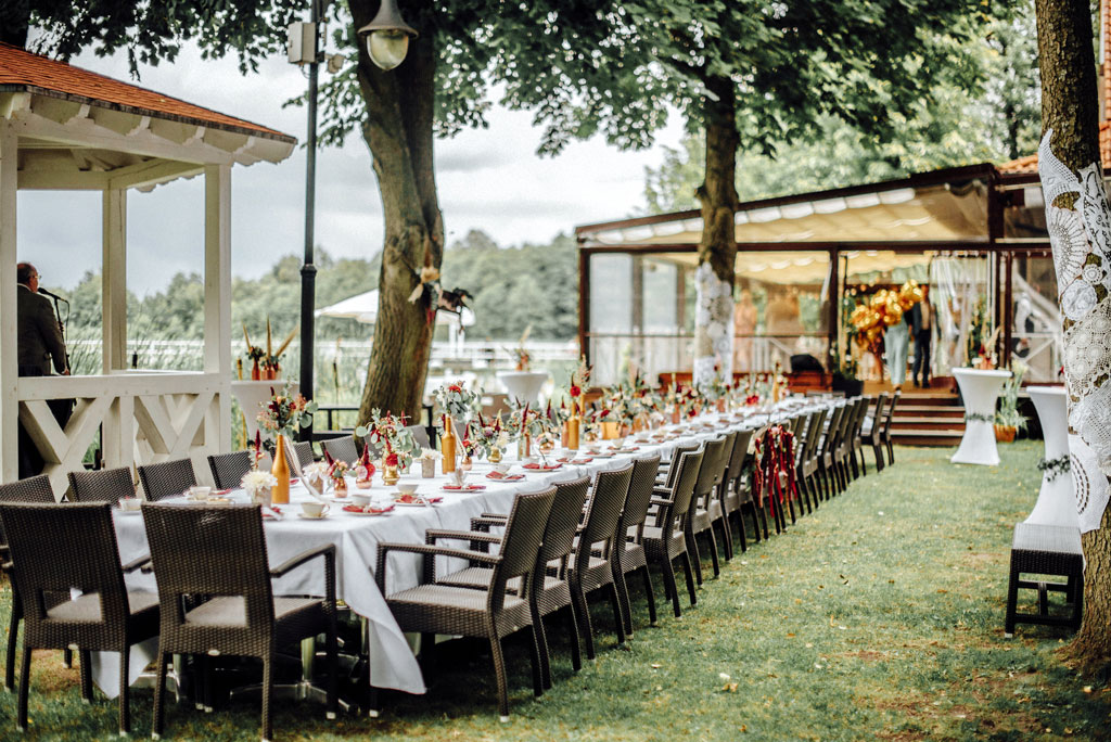 Langer, festlich gedeckter Tisch im Freien mit Hochzeitsdekoration, nahegelegener Pavillon und Blumenarrangements