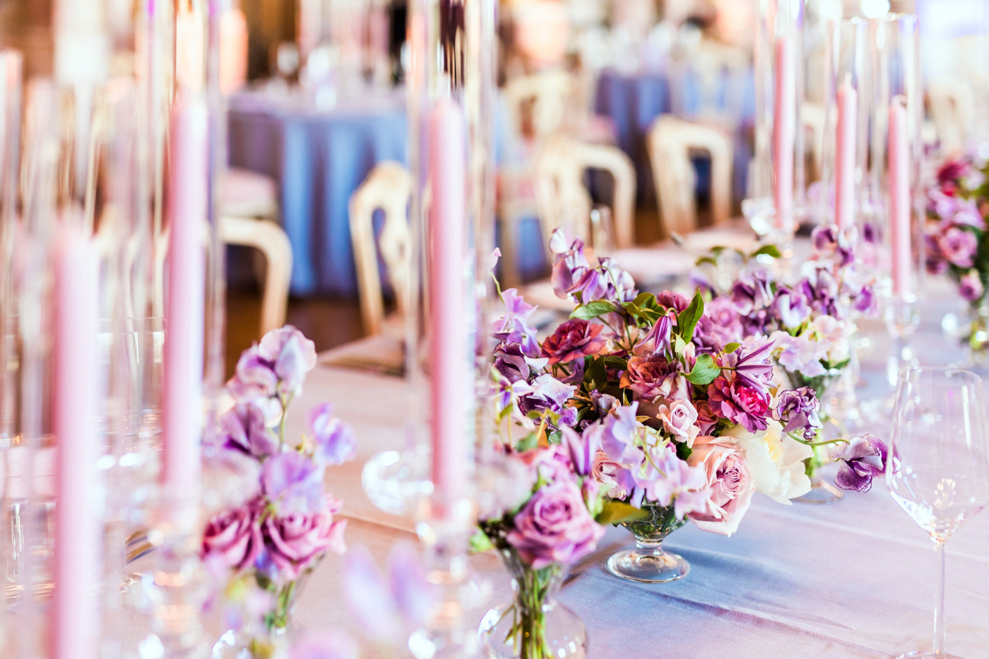 Detailreiche Hochzeitsdekoration mit violetten Blüten und Kerzen auf einer festlichen Tafel.