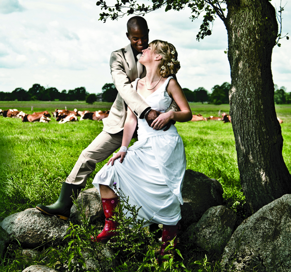 Braut und Bräutigam posieren in Hochzeitskleidung unter einem Baum auf dem Land.