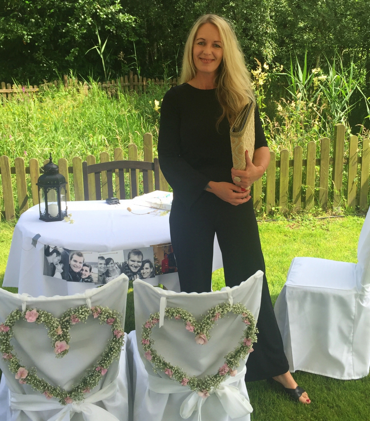 Blonde Frau steht neben festlich dekorierten Stühlen und Tisch im Garten für eine Hochzeit.