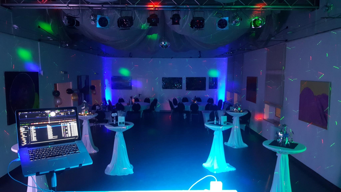 Eleganter Hochzeitsort mit stilvollem Lichtkonzept, Tischen für Hochzeitsgäste und DJ-Setup für die Feier.